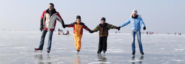 Eine Familie hält Händchen und läuft Schlittschuh auf einer Eisfläche.