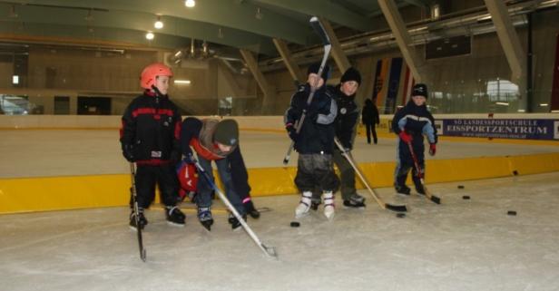 Eine Gruppe Kinder spielt Eishockey in einer Halle.