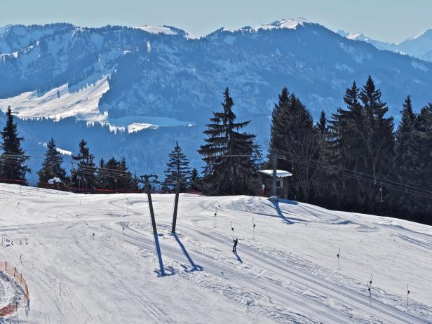 Ein Skifahrer fährt eine schneebedeckte Piste hinunter, im Hintergrund sind Berge zu sehen.