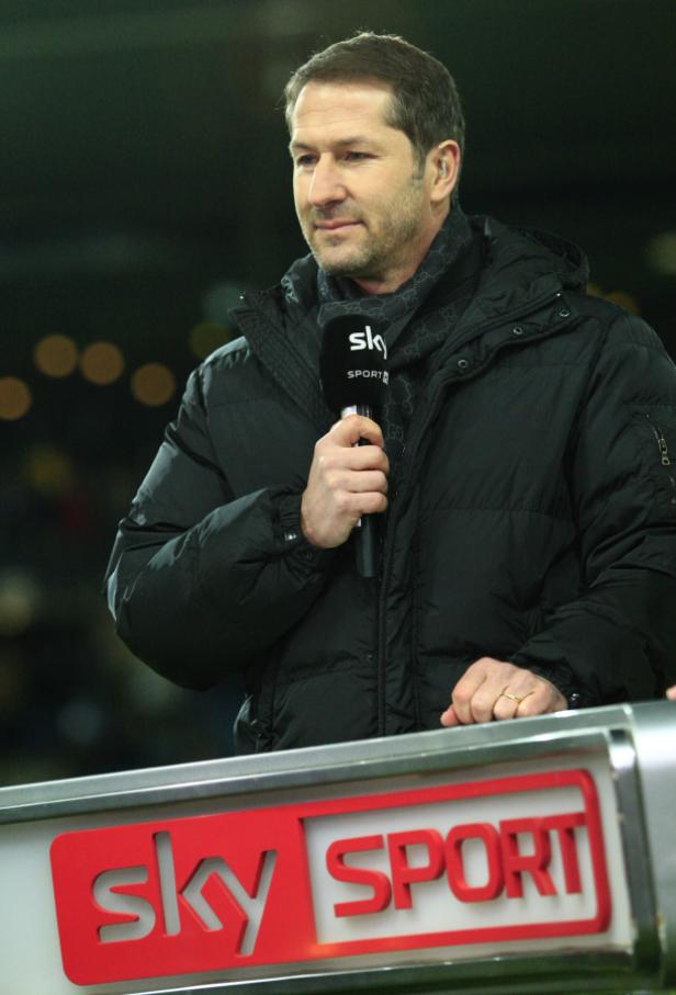 Ein Mann mit Mikrofon steht vor einem Sky Sport Logo.