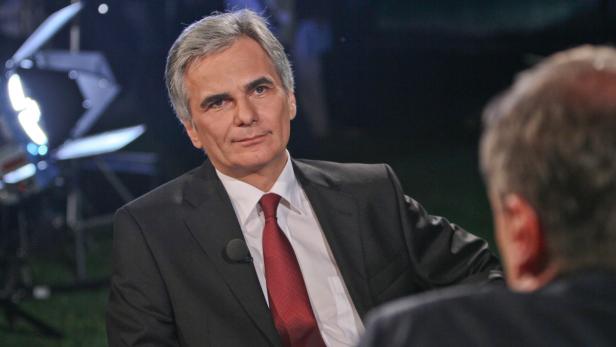 Ein Mann im Anzug sitzt in einem Fernsehstudio.