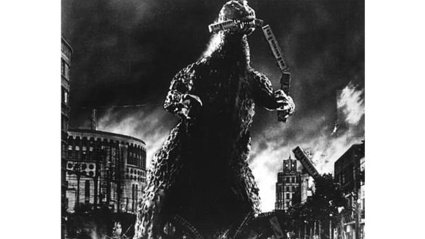 Godzilla hält in einem Schwarzweißbild eine zerstörte Eisenbahn in den Händen.