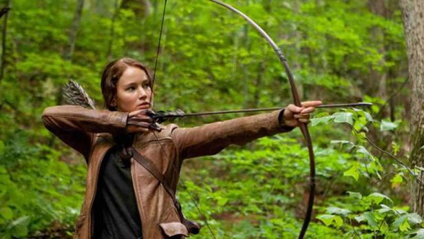 Jennifer Lawrence als Katniss Everdeen mit Pfeil und Bogen im Wald.