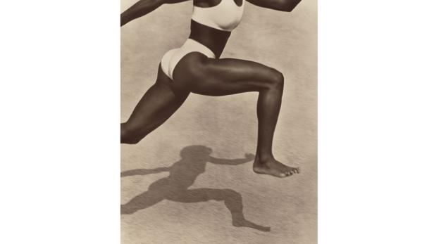 Eine barfüßige Frau in Sportkleidung springt und wirft einen Schatten.