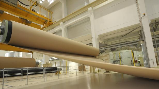 Eine große Papierrolle in einer Fabrikhalle wird abgerollt.