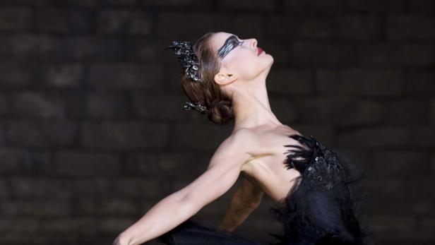 Eine Ballerina in einem schwarzen Tutu und mit dunklem Make-up blickt nach oben.