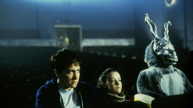 Jake Gyllenhaal und Jena Malone sitzen im Kino, neben ihnen eine Person im Hasenkostüm, vermutlich aus „Donnie Darko“.