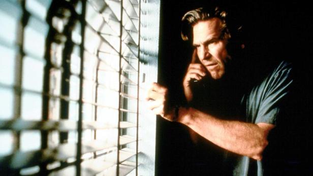 Ein Mann blickt durch eine Jalousie nach draußen.