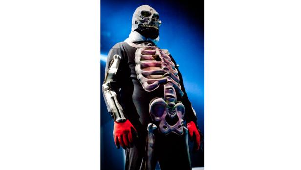 Eine Person in einem Skelettkostüm mit roten Handschuhen steht vor einem blauen Hintergrund.