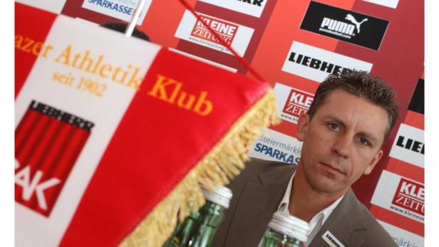 Ein Mann steht vor einer Wand mit Logos, darunter der Grazer Athletik Klub.