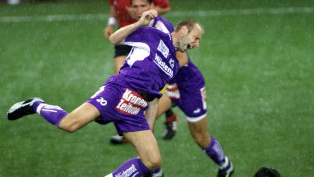 Ein Fußballspieler im lila Trikot stürzt während eines Spiels im Regen.