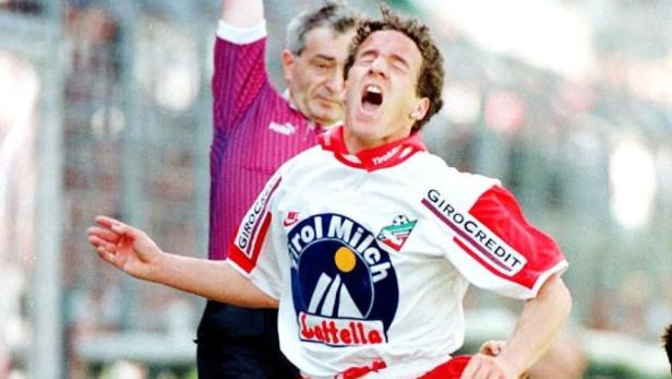 Ein Fußballspieler jubelt, während ein Schiedsrichter im Hintergrund eine Karte zeigt.