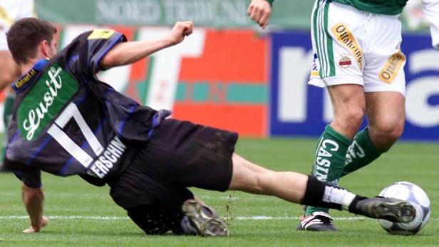 Ein Fußballspieler grätscht auf dem Rasen nach dem Ball.