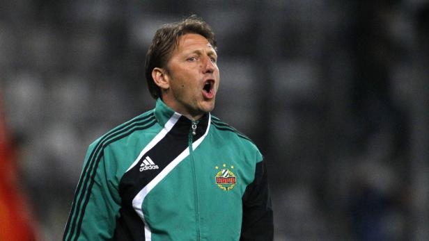 Ein Mann in einer grünen Jacke mit dem Rapid Wien-Logo ruft lautstark.