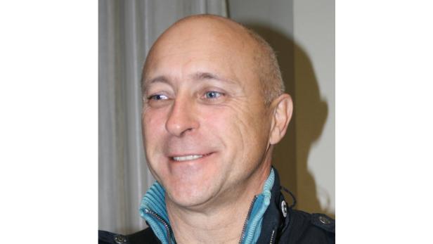 Ein lächelnder Mann mit blauen Augen und einer schwarzen Jacke.