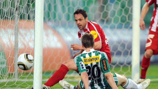 Ein Fußball landet im Netz, während zwei Spieler in rot und grün daneben stehen.