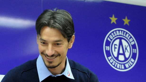 Ein lächelnder Mann vor dem Logo des Fussballklubs Austria Wien.