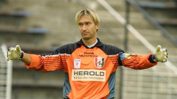 Ein Torwart in orangefarbenem Trikot mit ausgestreckten Armen.