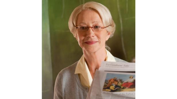 Helen Mirren hält eine Zeitung mit einem religiösen Bild darauf.