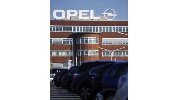 Das Opel-Logo auf einem Backsteingebäude über einer Reihe geparkter Autos.