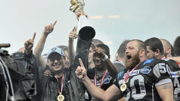 Eine Gruppe von American-Football-Spielern feiert mit einem Pokal ihren Sieg.