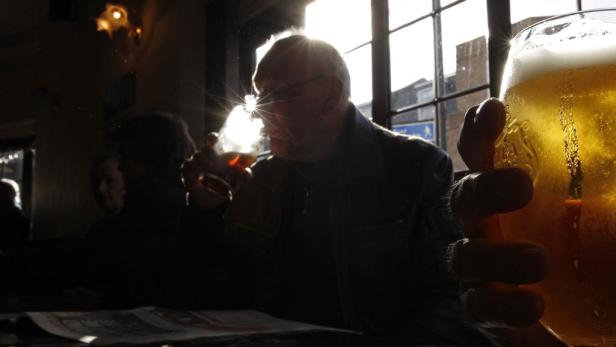Ein Mann sitzt in einem dunklen Raum und hält ein Glas Bier hoch.