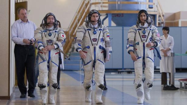Drei Astronauten in Raumanzügen gehen in einer Halle.