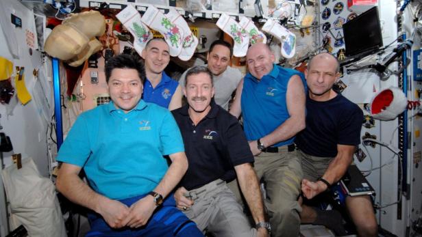Sechs Astronauten posieren in der Internationalen Raumstation vor Weihnachtsstrümpfen.