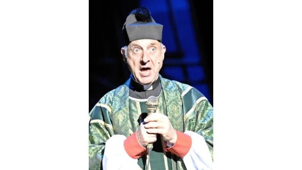 Ein Mann im Priesterkostüm hält ein Mikrofon und schaut überrascht.