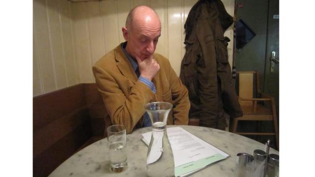 Ein Mann sitzt an einem Tisch in einem Café und liest eine Speisekarte.