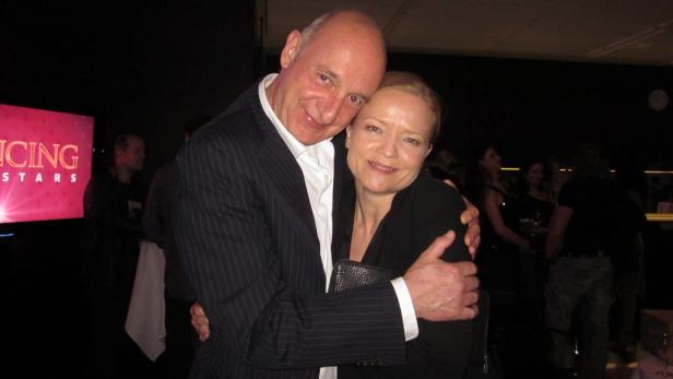 Ein Mann im Anzug umarmt eine Frau vor dem Hintergrund einer „Dancing Stars“-Veranstaltung.