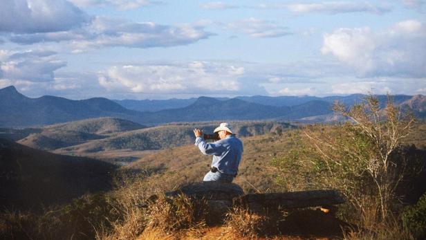Ein Mann mit Hut fotografiert die hügelige Landschaft.