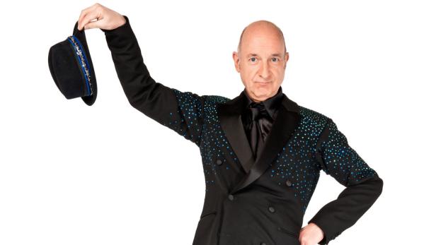 Ein Mann im glitzernden Anzug hält einen Hut in der Hand.