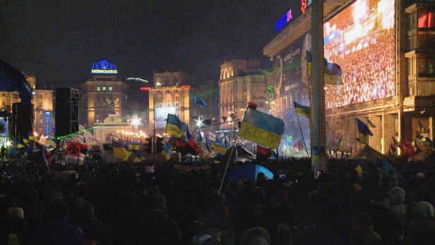Eine Menschenmenge demonstriert nachts auf dem Maidan-Platz in Kiew mit ukrainischen Flaggen.