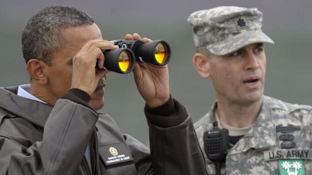 Barack Obama blickt durch ein Fernglas, neben ihm ein Soldat in Uniform.