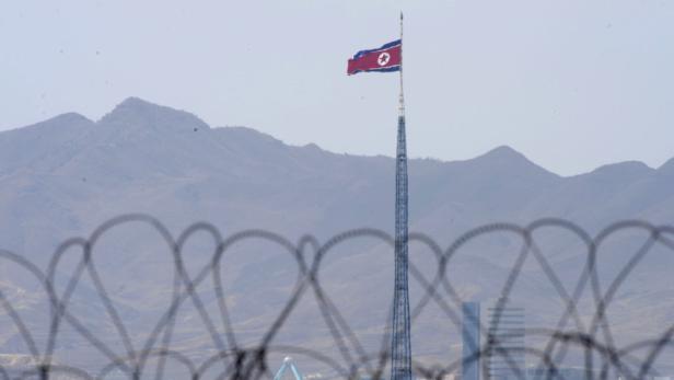 Eine nordkoreanische Flagge weht auf einem hohen Mast vor einer Bergkulisse.