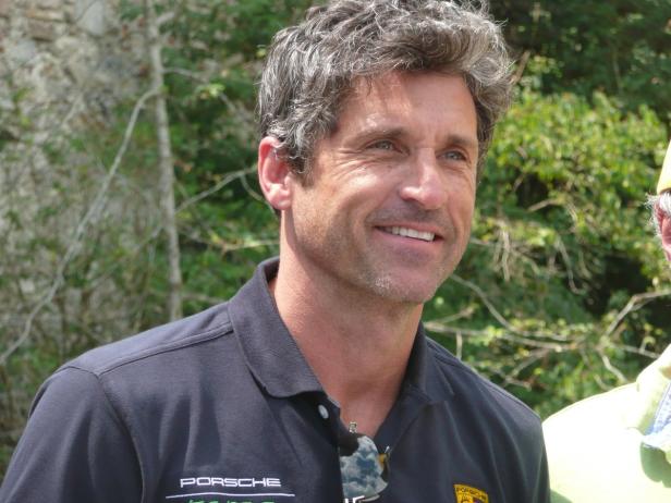 Patrick Dempsey trägt ein Porsche-Polohemd und lächelt.