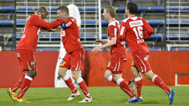 Mehrere Fußballspieler in roten Trikots feiern auf dem Spielfeld.