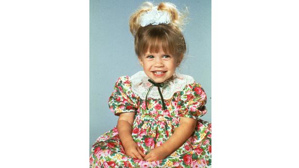 Ein lächelndes kleines Mädchen in einem geblümten Kleid mit weißer Spitze.