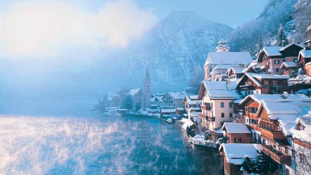 Winterliche Ansicht von Hallstatt am See mit schneebedeckten Häusern und Bergen.
