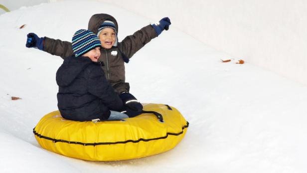 Zwei Kinder haben Spaß beim Rodeln mit einem gelben Reifen im Schnee.