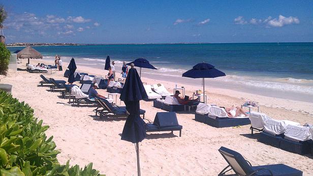 Menschen entspannen sich an einem sonnigen Strand unter blauen Sonnenschirmen.