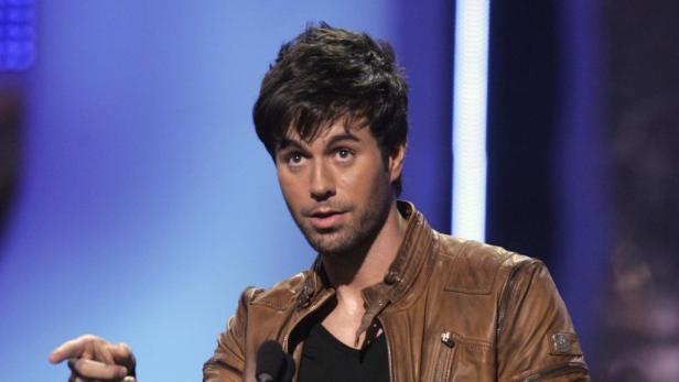 Enrique Iglesias in einer braunen Lederjacke vor einem blauen Hintergrund.