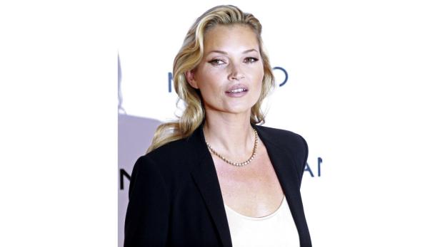 Kate Moss trägt ein schwarzes Jackett und eine Halskette.