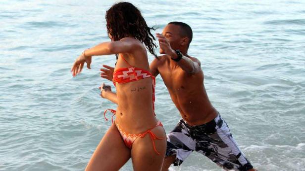 Eine Frau im Bikini und ein Mann stehen im flachen Wasser am Strand.