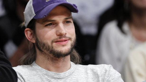 Ashton Kutcher mit Bart und Baseballkappe, während eines Basketballspiels.