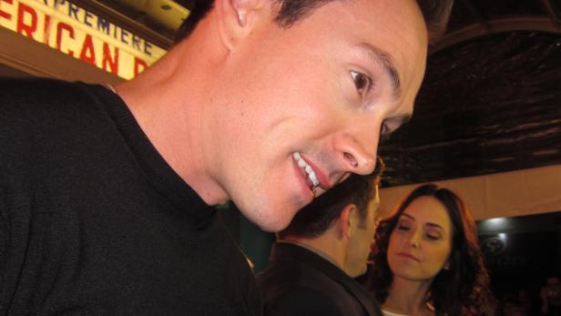 Ein Mann im schwarzen Pullover auf einer Veranstaltung, im Hintergrund eine Frau.