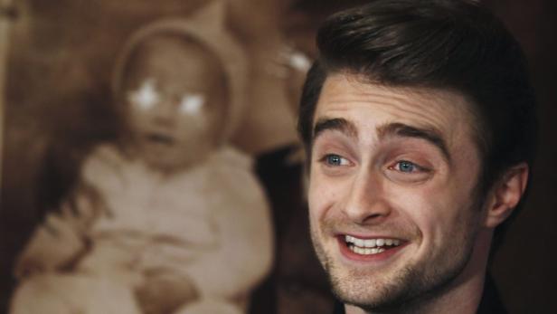 Daniel Radcliffe lächelt vor einem alten Foto eines Babys.