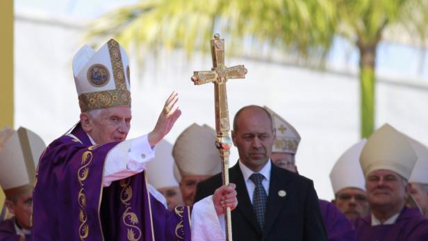 Papst Benedikt XVI. winkt mit einem goldenen Kreuz in der Hand.