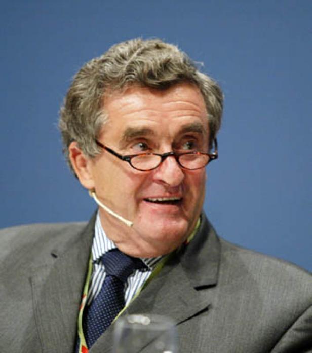 Ein Mann mit Brille und grauem Haar trägt einen Anzug und ein Mikrofon.
